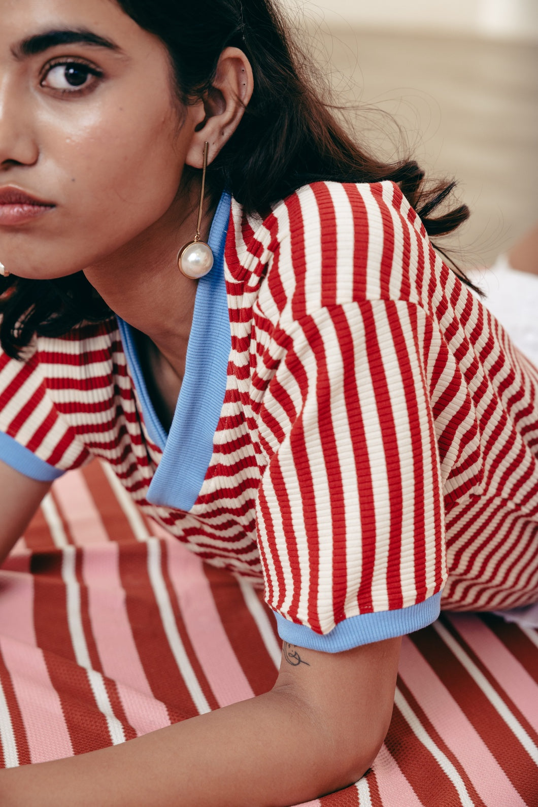 Person wearing a red and white striped shirt with a blue trim, sitting on a striped surface.