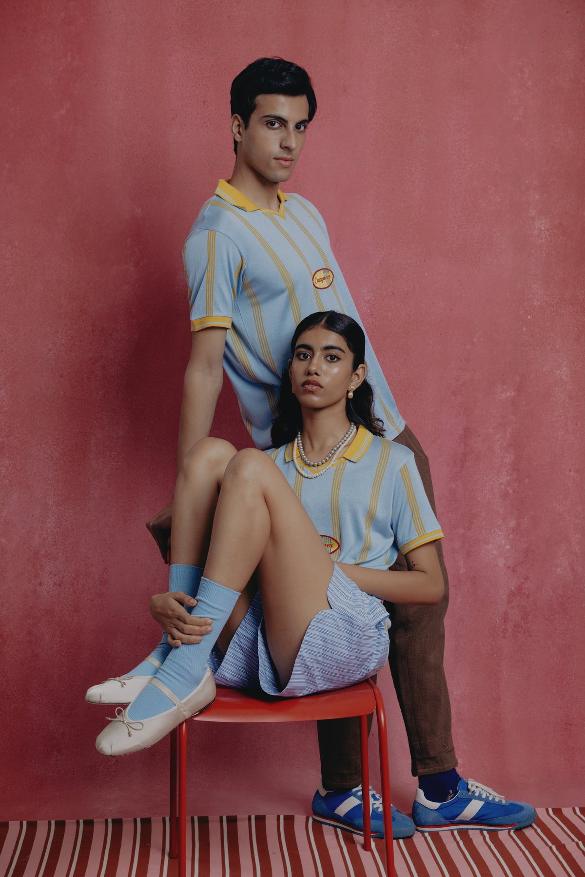 Two people wearing matching blue and yellow outfits against a pink background