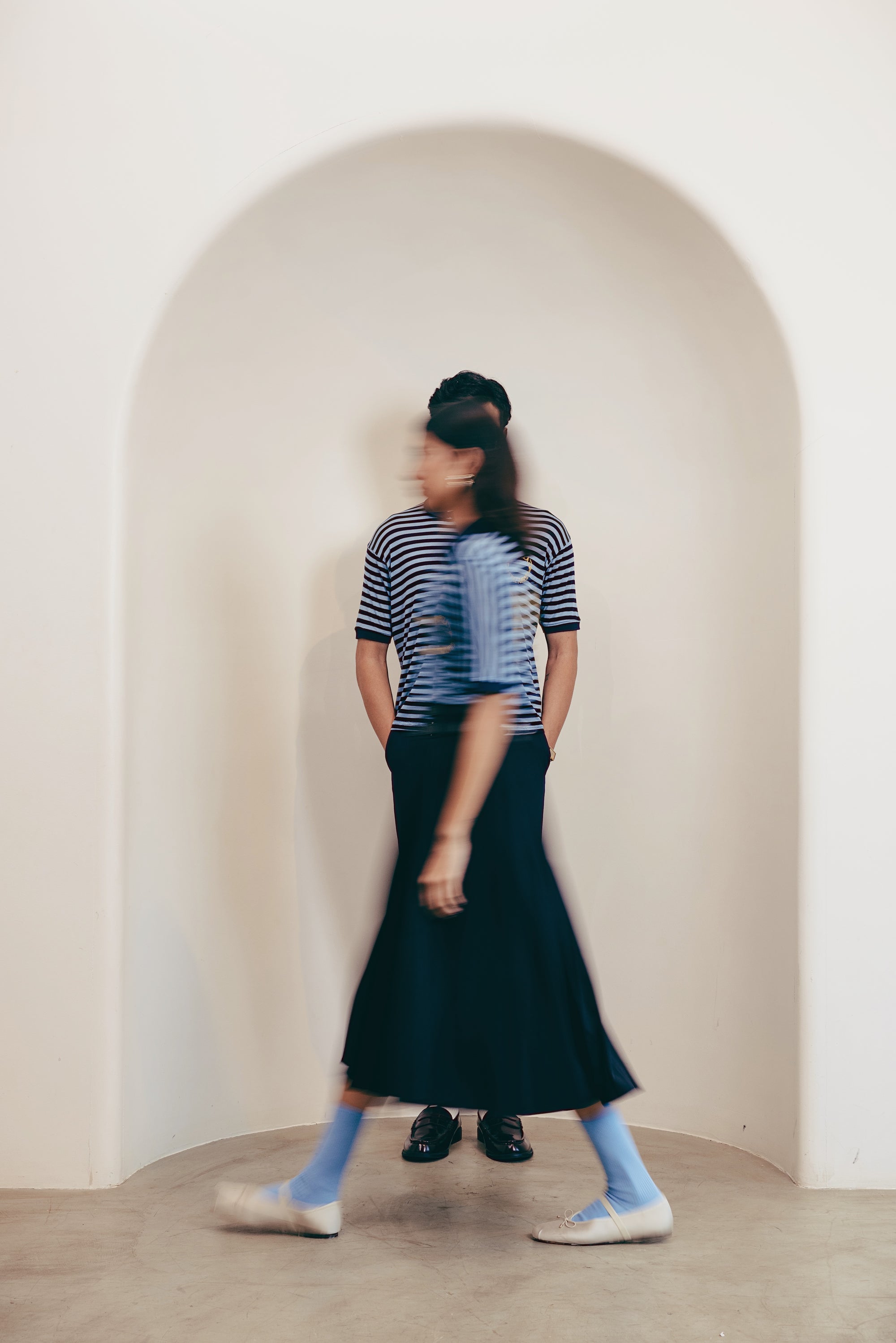 Person wearing a striped shirt and black skirt standing in front of an archway.