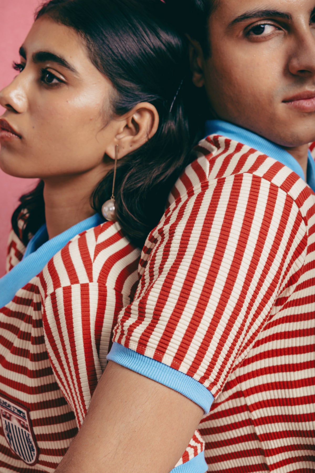 Two people wearing candy cane striped shirts with blue trim against a pink background