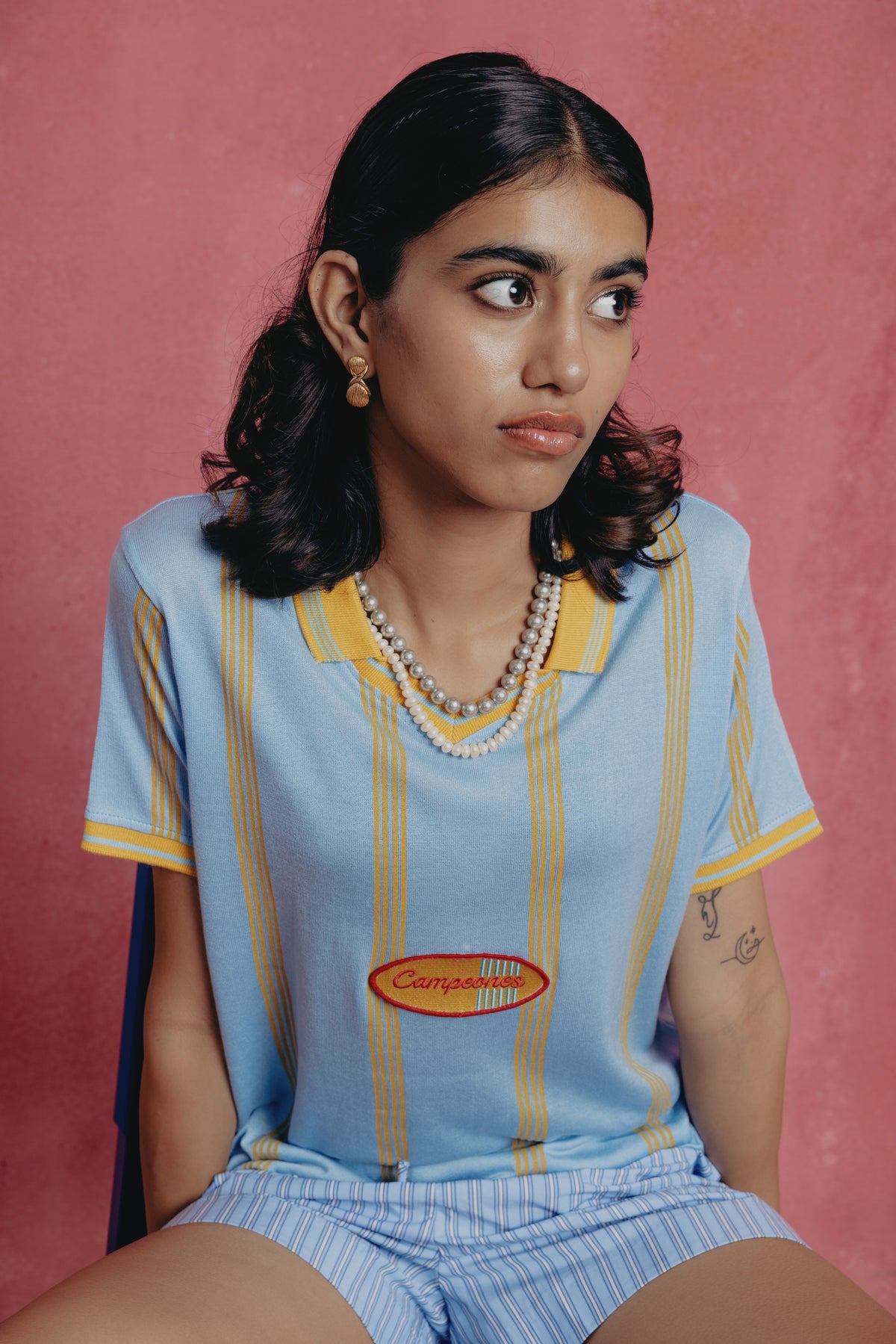 Girl wearing a light blue striped shirt with a logo and matching shorts against a pink background